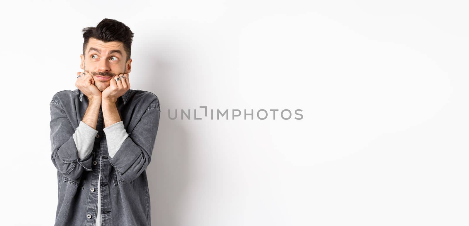 Excited cute young man look dreamy at upper left corner, waiting for parcel, daydreaming or imaging something, standing on white background.