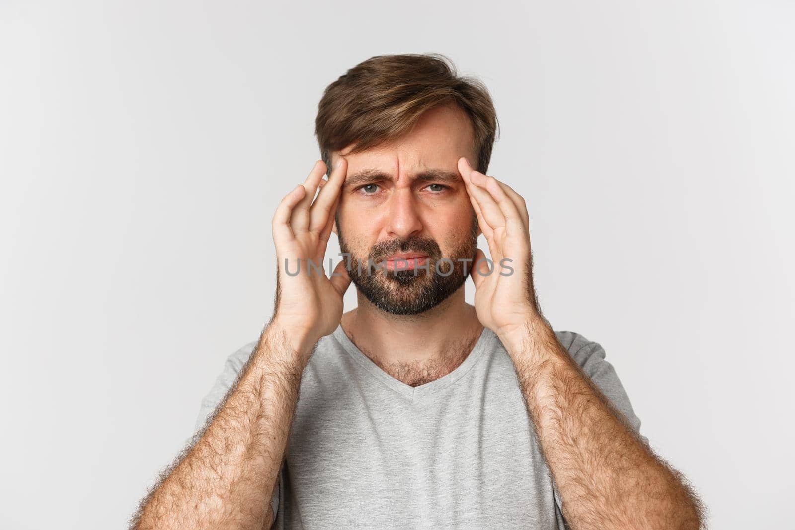 Close-up of gloomy bearded man, touching head and grimacing, having a headache or migraine, standing over white background.