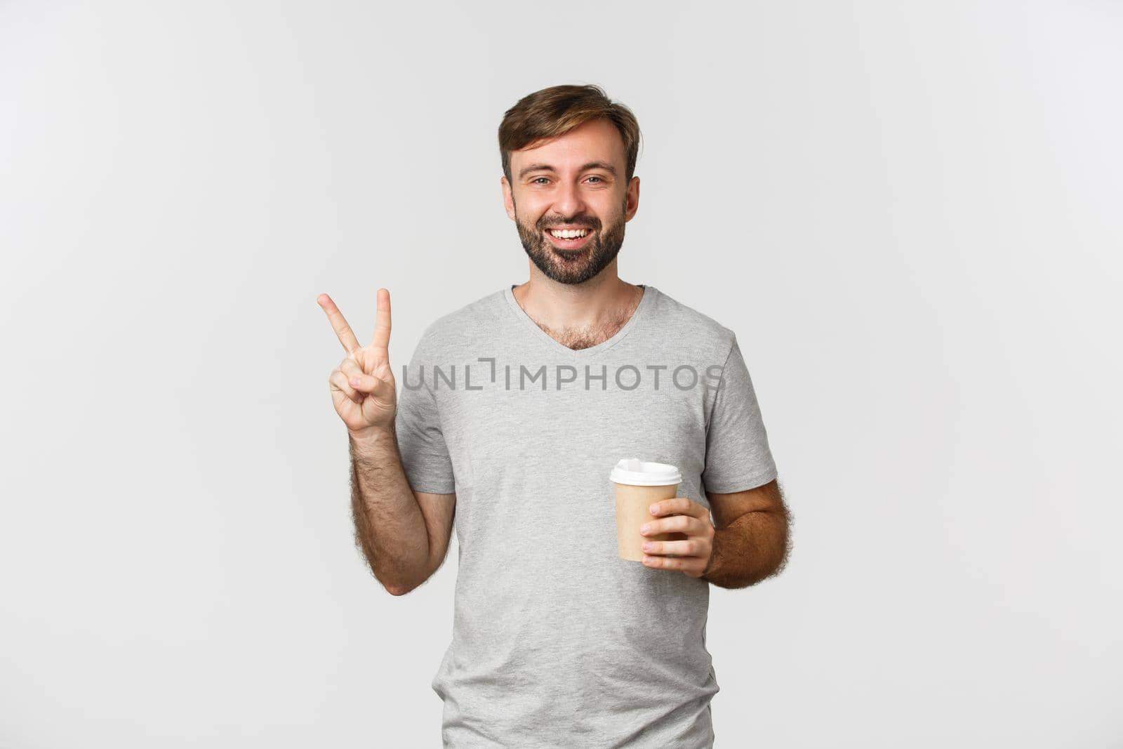 Image of happy guy drinking takeaway coffee, showing peace sign and smiling, standing over white background by Benzoix