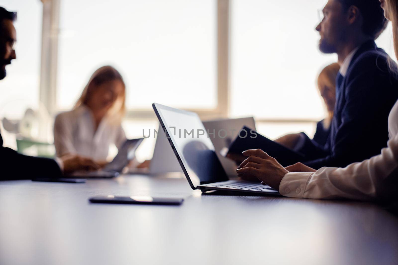 Group of business people working with laptop computers in office against of windows on blurred background. Selective focus on female hands typing in foreground. Toned image.