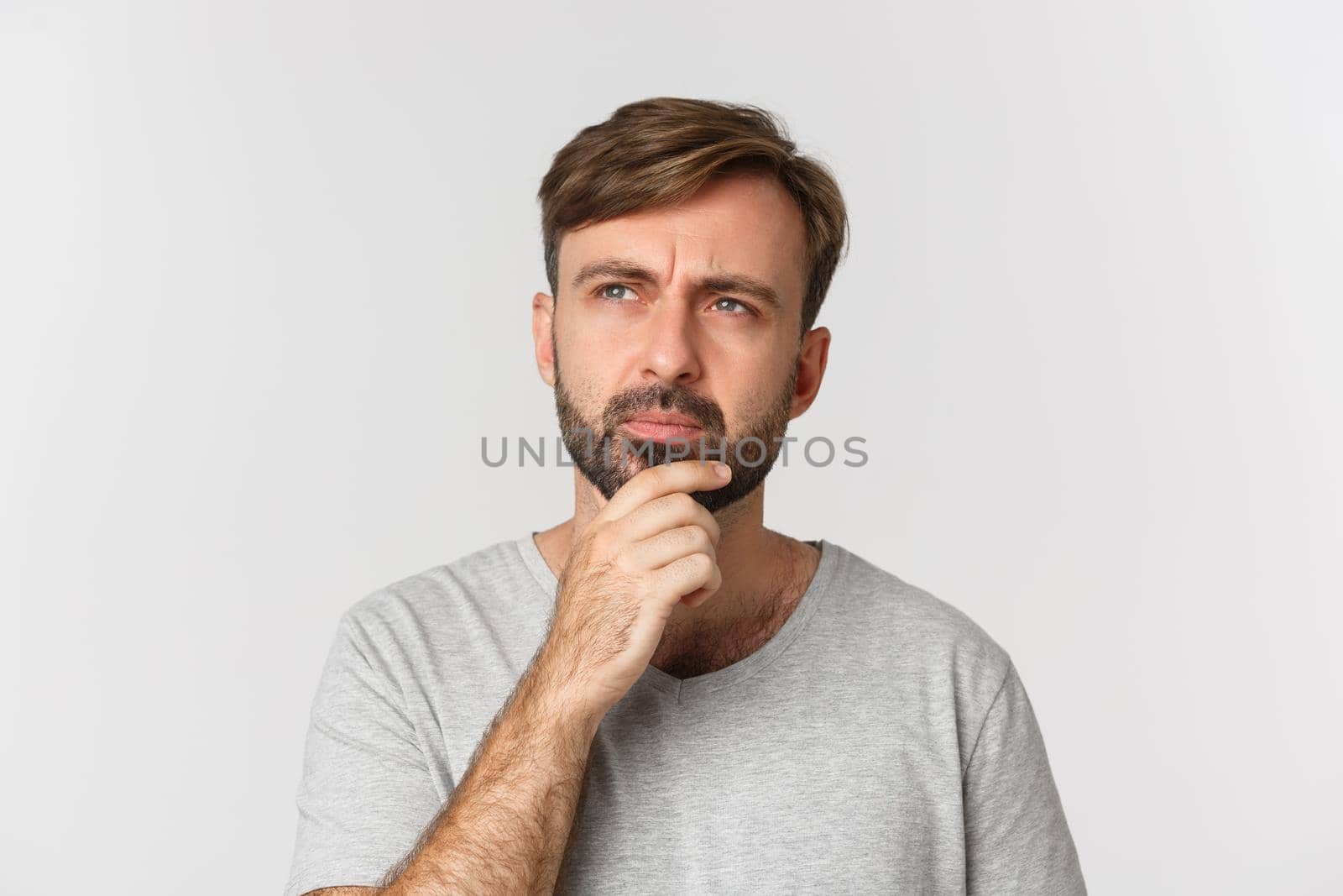Close-up of thoughtful serious man with beard, thinking and looking at upper left corner, making decision, standing over white background.