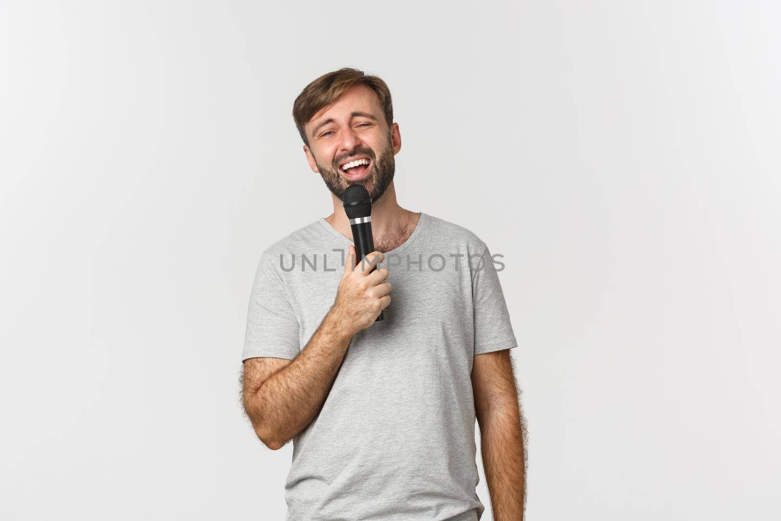 Handsome carefree guy singing song in karaoke, holding microphone, standing over white background by Benzoix