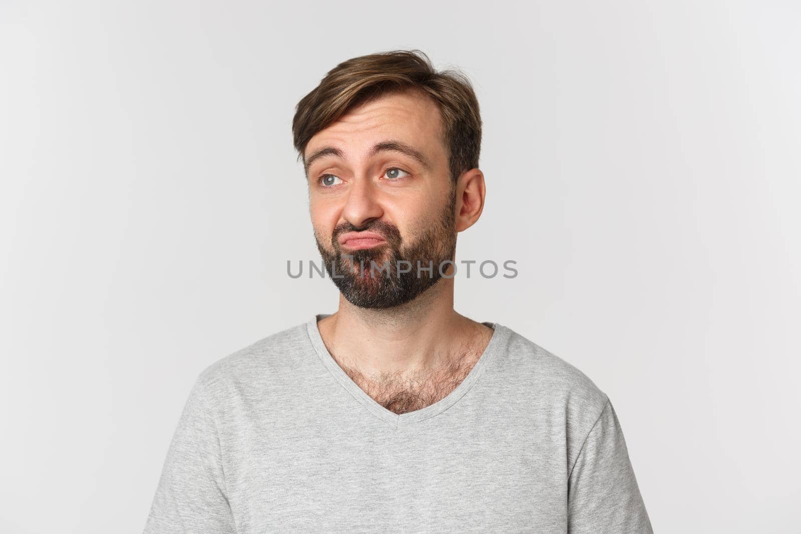 Close-up of skeptical caucasian guy with beard, looking upset left and pouting, standing over white background by Benzoix