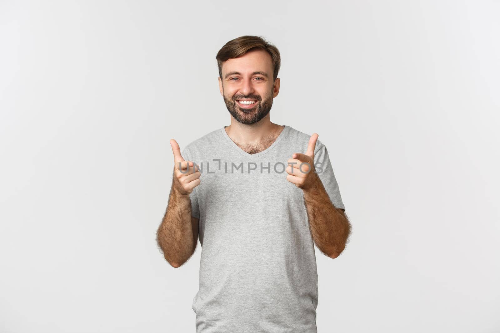 Image of satisfied smiling man in gray t-shirt, showing thumbs-up in approval, like something good, white background.