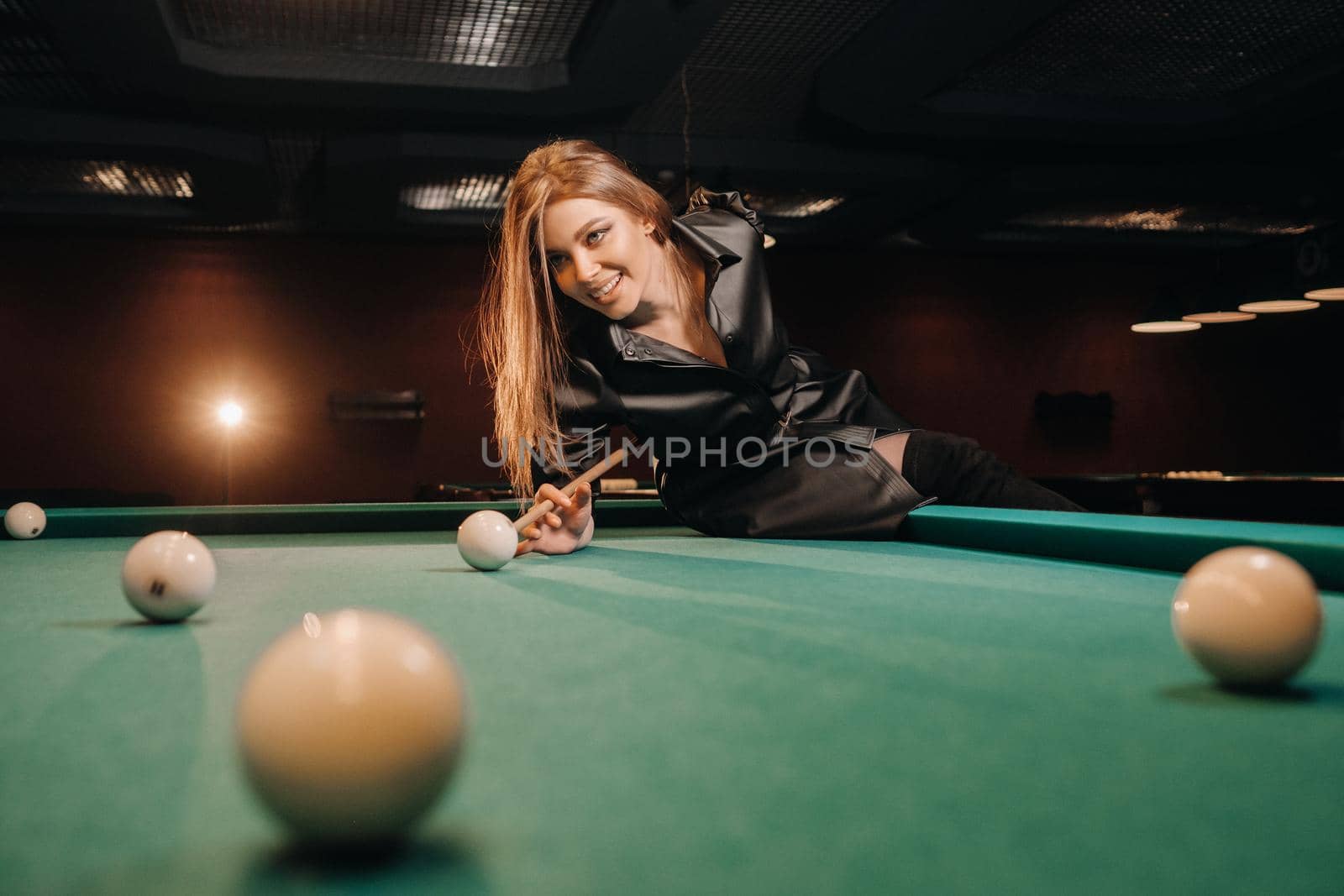 A girl with a cue in her hands makes a shot at a ball in a billiard club.Russian billiards.
