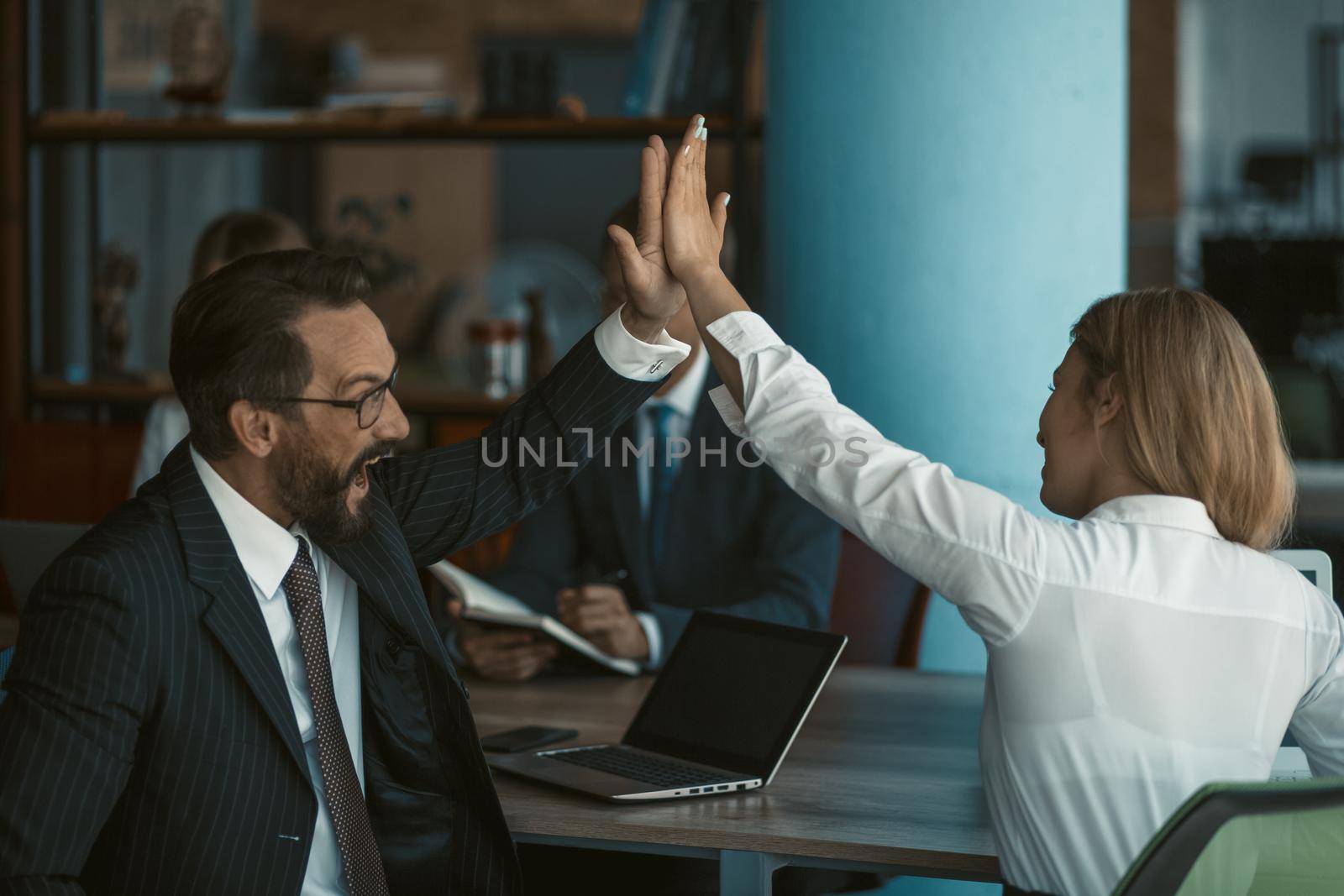 Office workers give high five each other. Happy business man and woman join their hands together sitting at office table with laptop computer on it. Toned image.