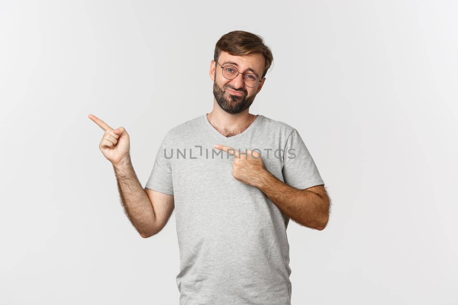 Skeptical and unamused bearded man smirking, pointing fingers at upper left corner, showing logo, standing over white background by Benzoix