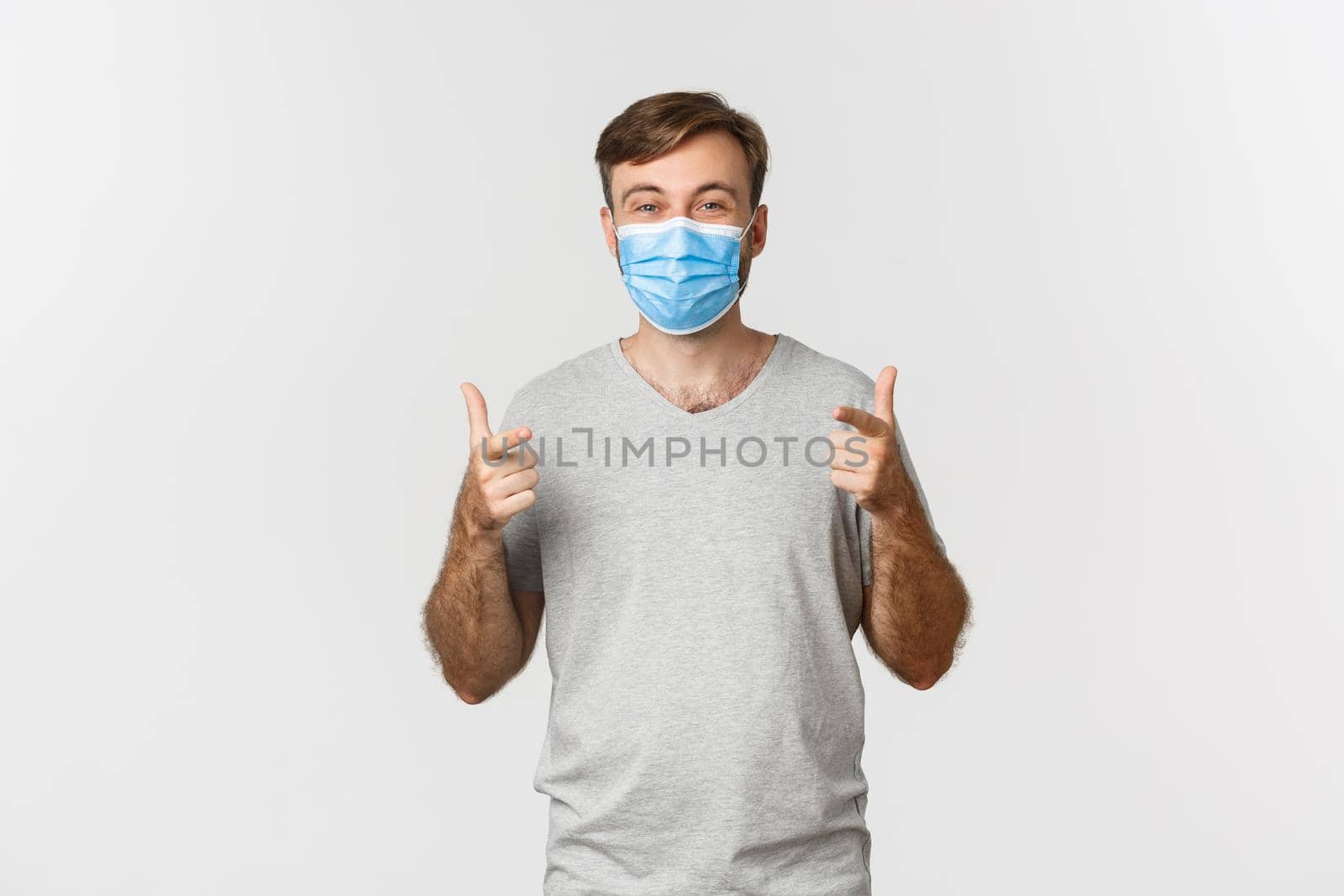 Concept of pandemic, coronavirus and social-distancing. Excited handsome man in gray t-shirt and medical mask, showing thumbs-up and smiling, liking something good by Benzoix
