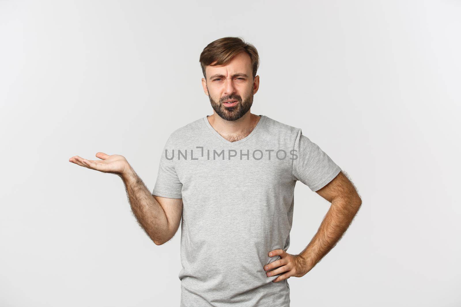 Portrait of confused and annoyed guy arguing, raising hand up and looking puzzled, standing over white background.