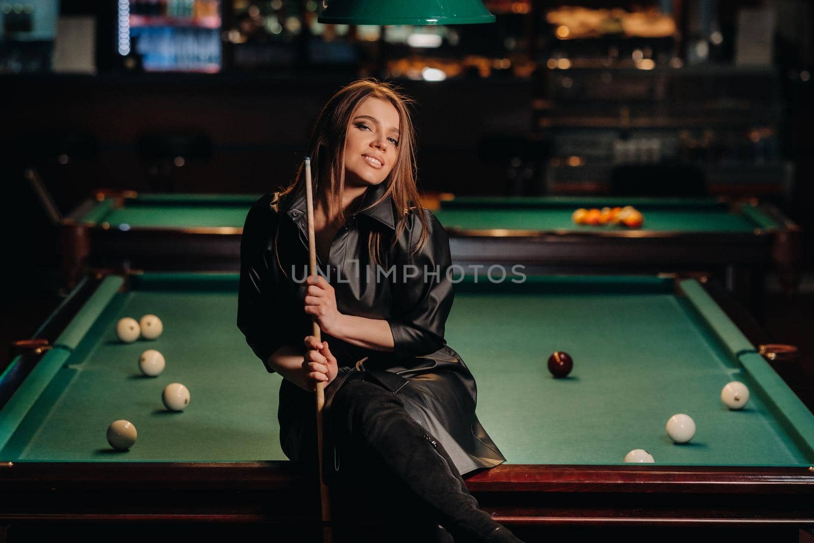A girl with a cue in her hands sits on a table in a billiard club.Russian billiards.