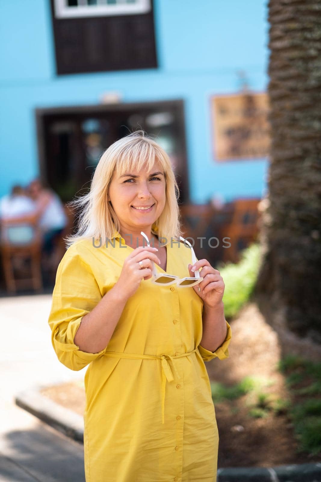 a blonde woman in a yellow summer dress stands on the street of the Old town of La Laguna on the island of Tenerife.Spain, Canary Islands by Lobachad