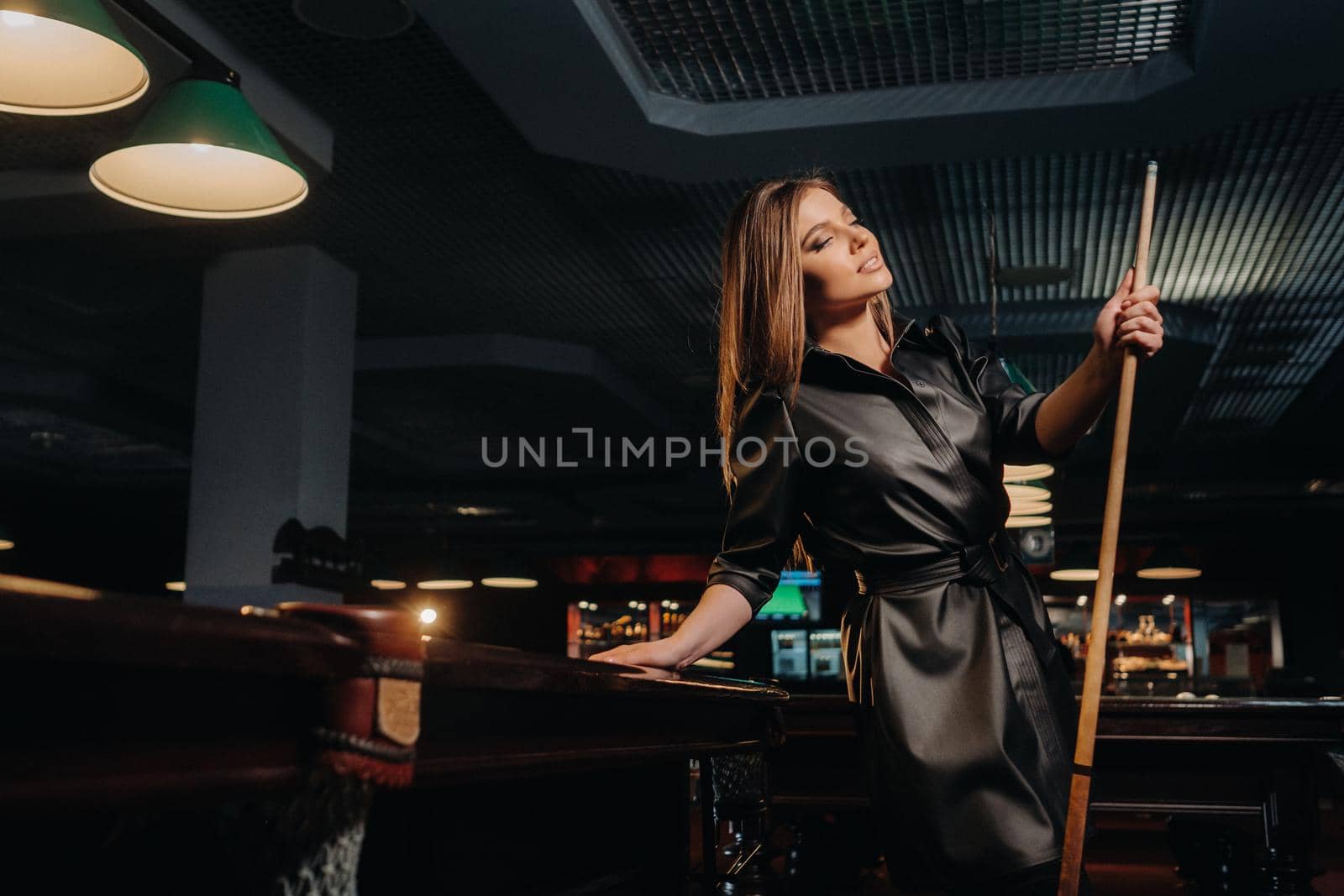A girl with a cue in her hands is standing in a billiard club.Russian billiards by Lobachad