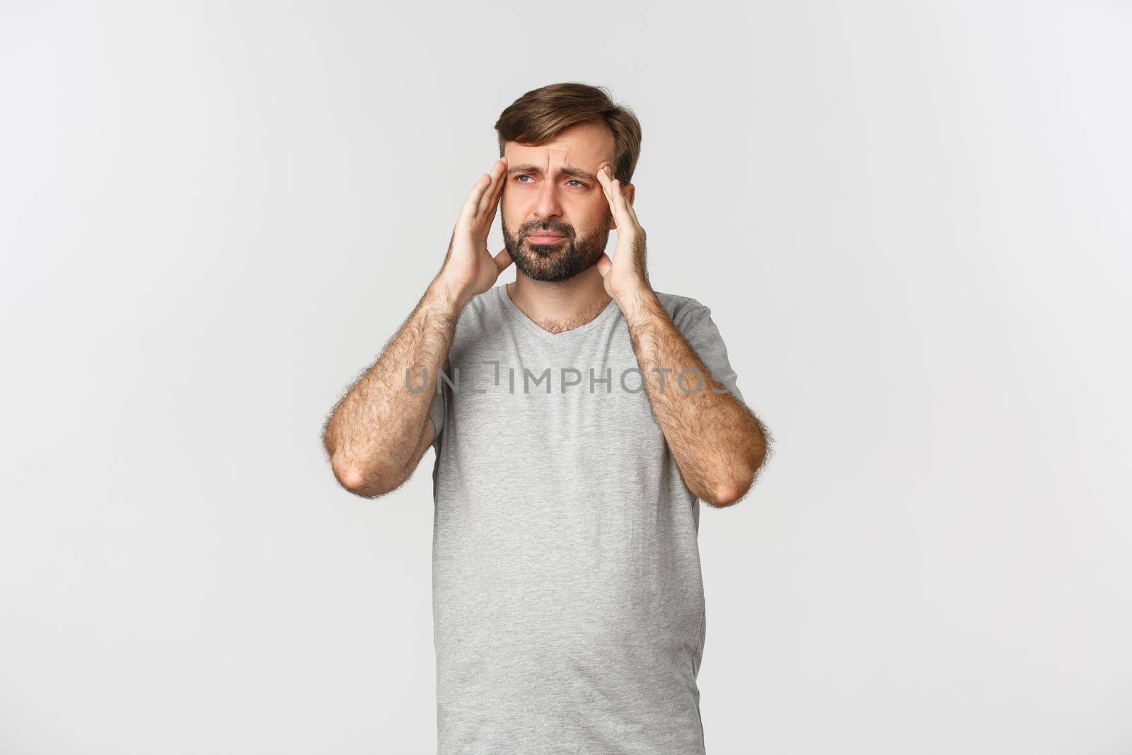Man having a severe headache, grimacing and touching head, feeling dizzy or sick, standing in gray t-shirt over white background.