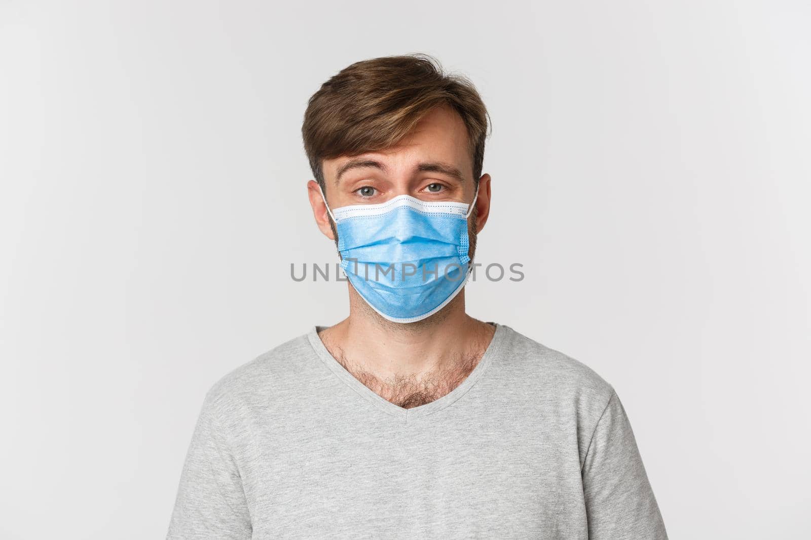 Concept of pandemic, covid-19 and social-distancing. Close-up of skeptical guy in medical mask, raising eyebrow and looking unamused, standing over white background.