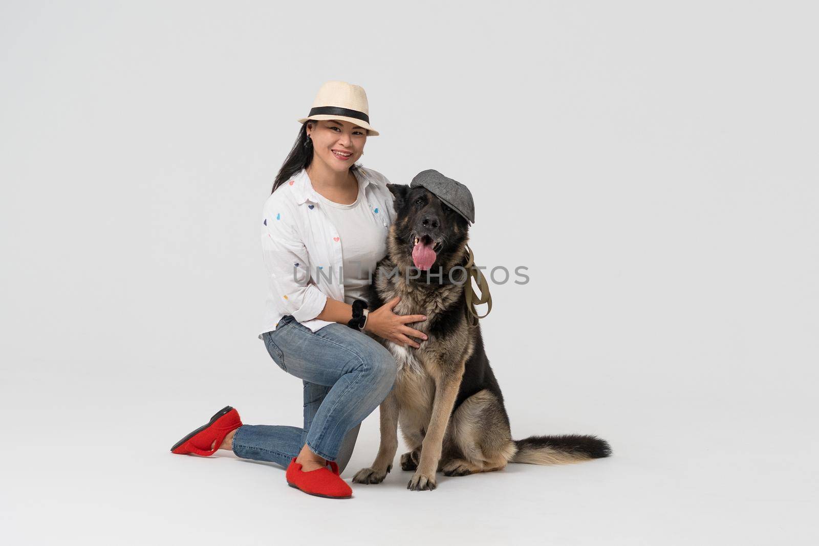 Funny Dog and hostess in hats. Woman in hat and Eastern European Shepherd wearing cap posing on white background. Pet concept.