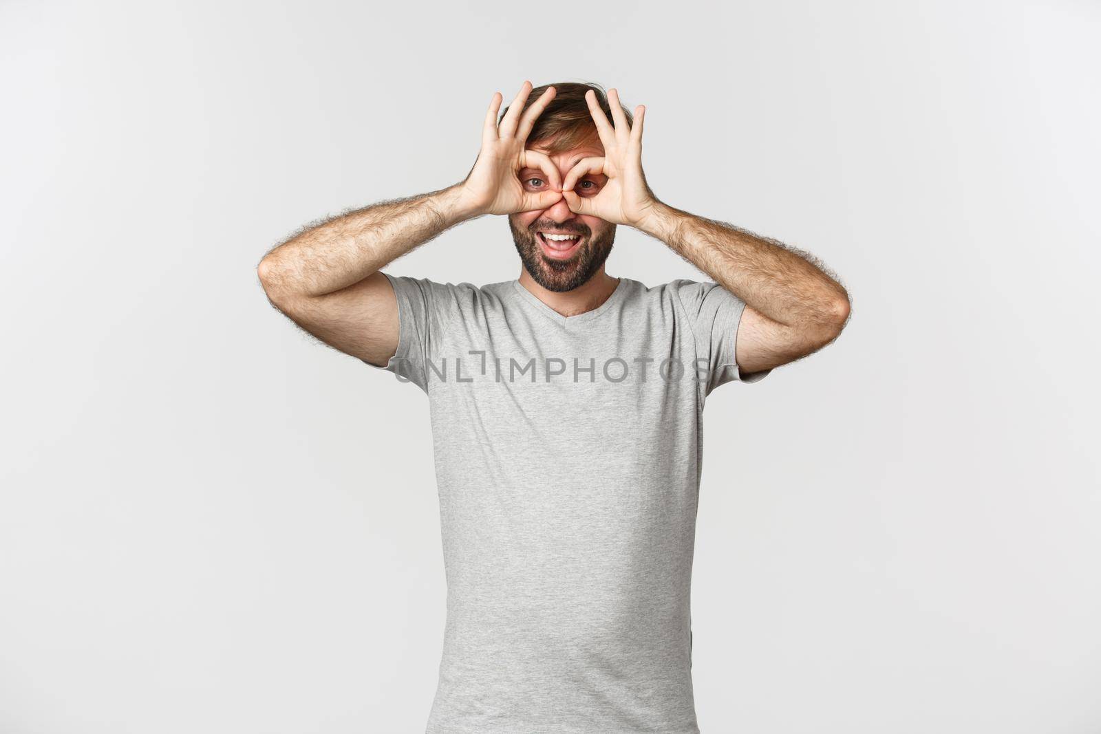 Portrait of funny caucasian guy making faces and mocking someone, standing over white background.