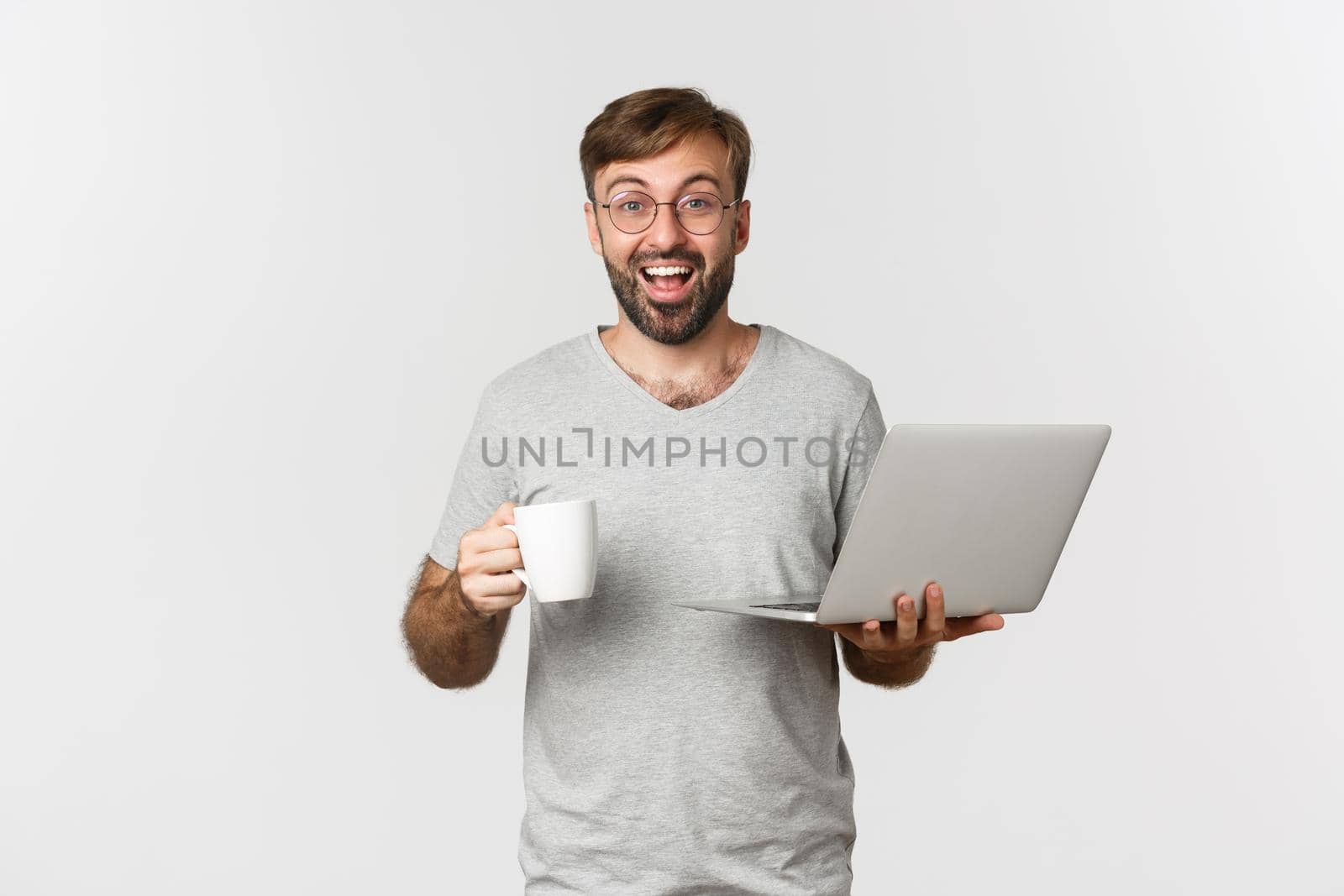 Young happy man working with laptop, drinking coffee and smiling, standing over white background.