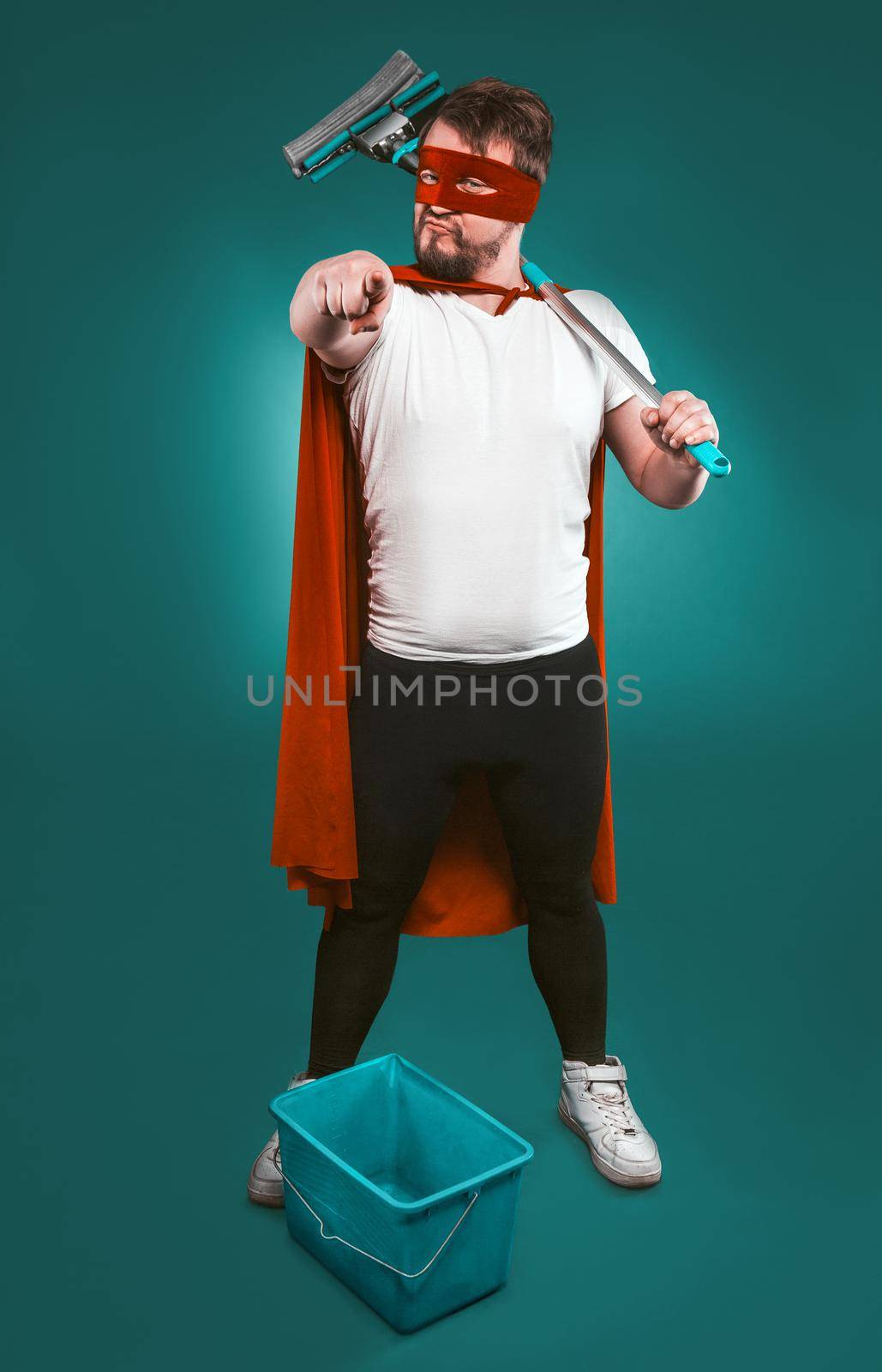 Superhero is ready to fight for cleanliness, Brave man in a red superhero uniform with a bucket and a mop points the camera with his index finger. Cleaning concept. Isolated on green by LipikStockMedia