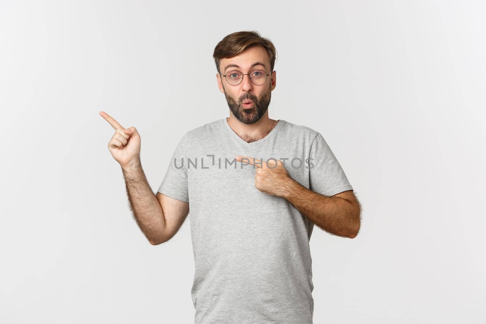 Surprised bearded man smiling, pointing fingers at upper left corner, showing logo, standing over white background by Benzoix