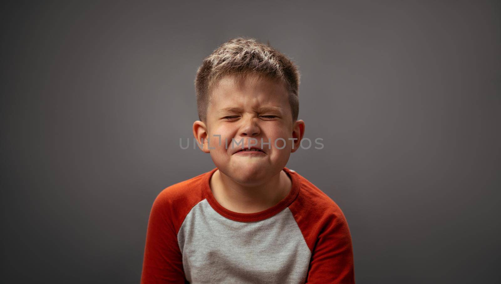 Little kid grimaces and closed his eyes. Preschool boy expresses unwillingness to brush his teeth. Emotions concept by LipikStockMedia