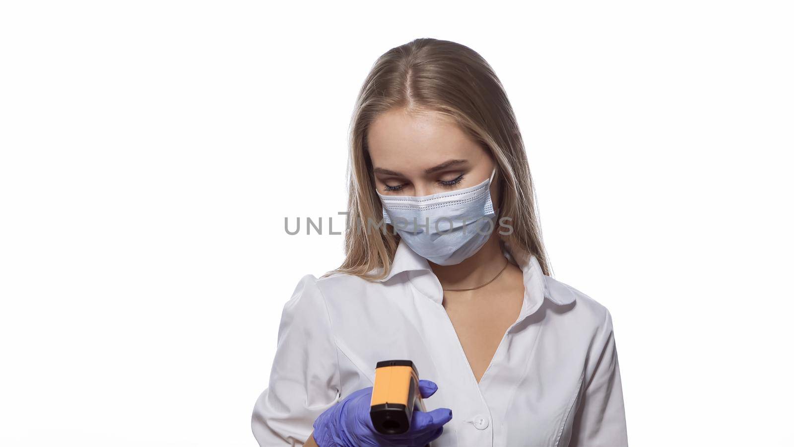 Young health inspector looks at the display of a thermometer monitor and checks the body temperature of visitors or office workers. Isolated on white background.