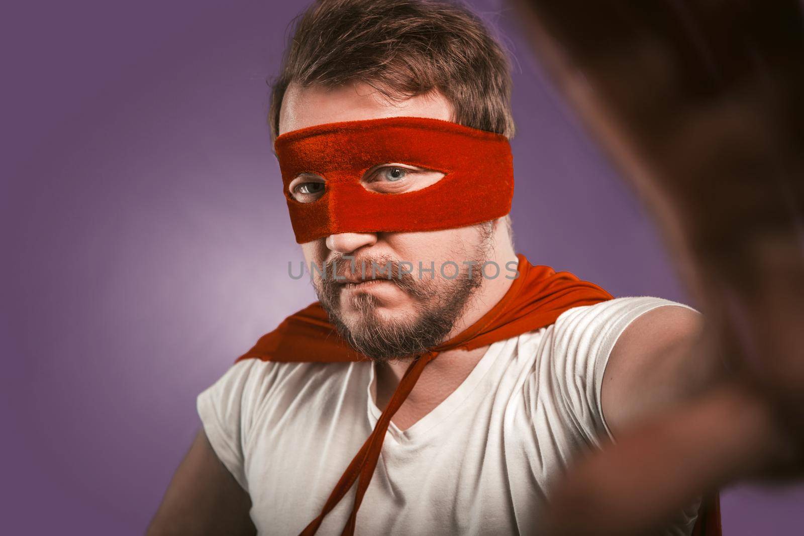 Superhero makes selfie photo by mobile phone for his blog, fans and followers. Close up portrait of serious man wearing red mask and cloak looking at camera by LipikStockMedia