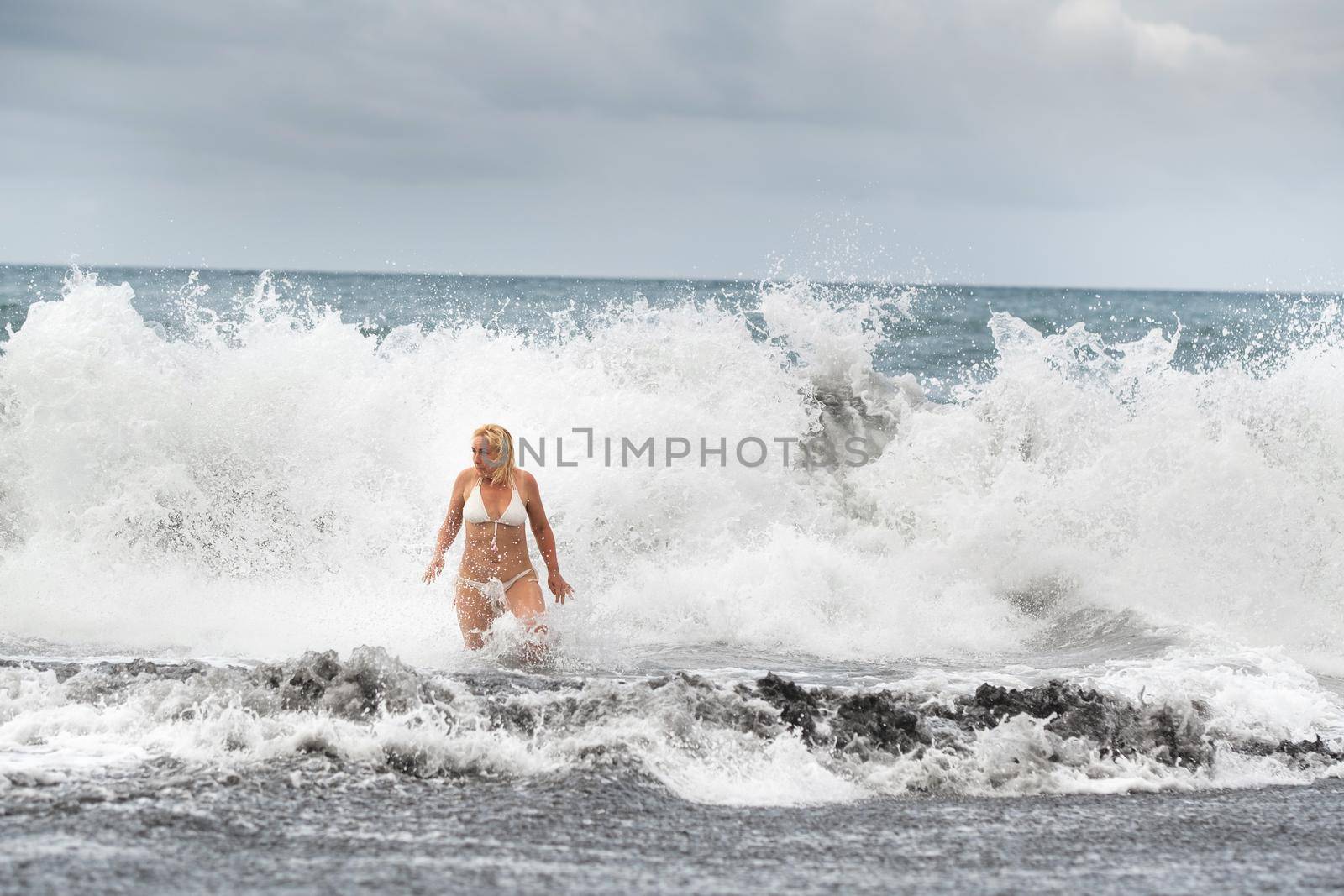 A girl with wet hair jumps over large waves in the Atlantic ocean, around a wave with splashes of spray and water drops.Tenerife.Spain.