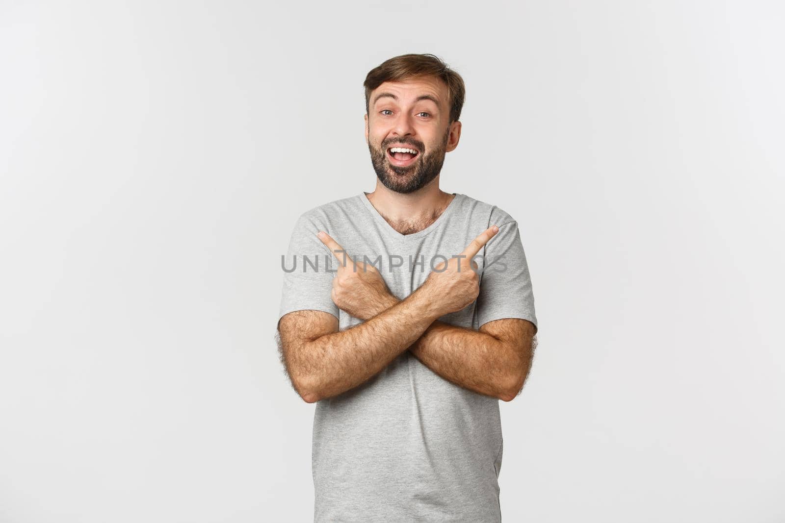 Portrait of happy and amazed bearded male model in gray t-shirt, pointing fingers sideways, showing two good choices, standing over white background by Benzoix