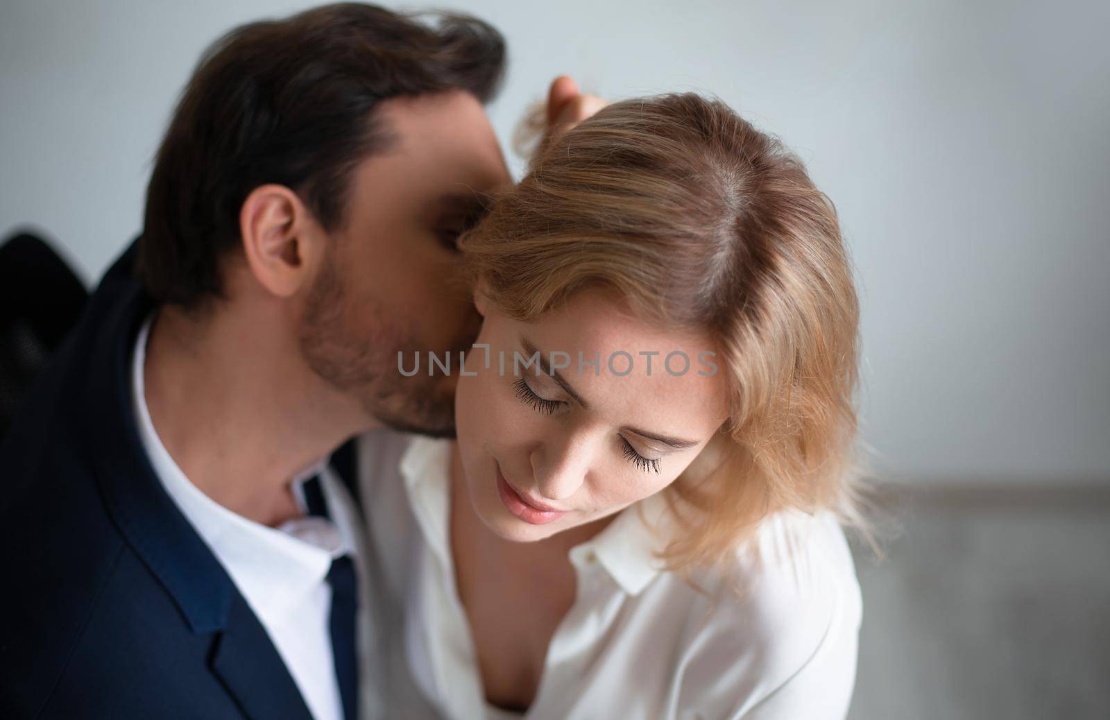 Business man kissing neck of young blonde woman closed eyes. Passion kiss. Enjoyment or workplace romance concept by LipikStockMedia
