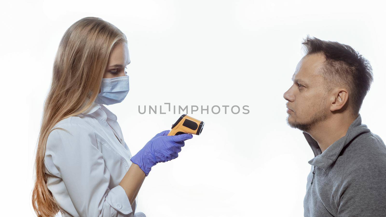 A young nurse looks at the display of a thermometer monitor and checks the body temperature of visitors or office workers. Isolated on white background.