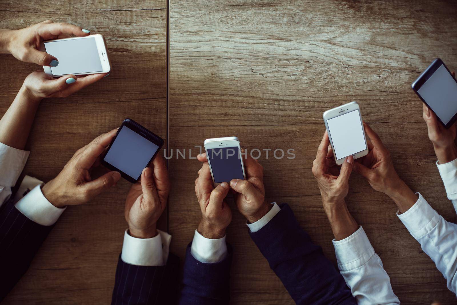 Business people using mobile phones. Human hands holding smartphones with empty screens on wooden desk background. High angle view. Toned image.