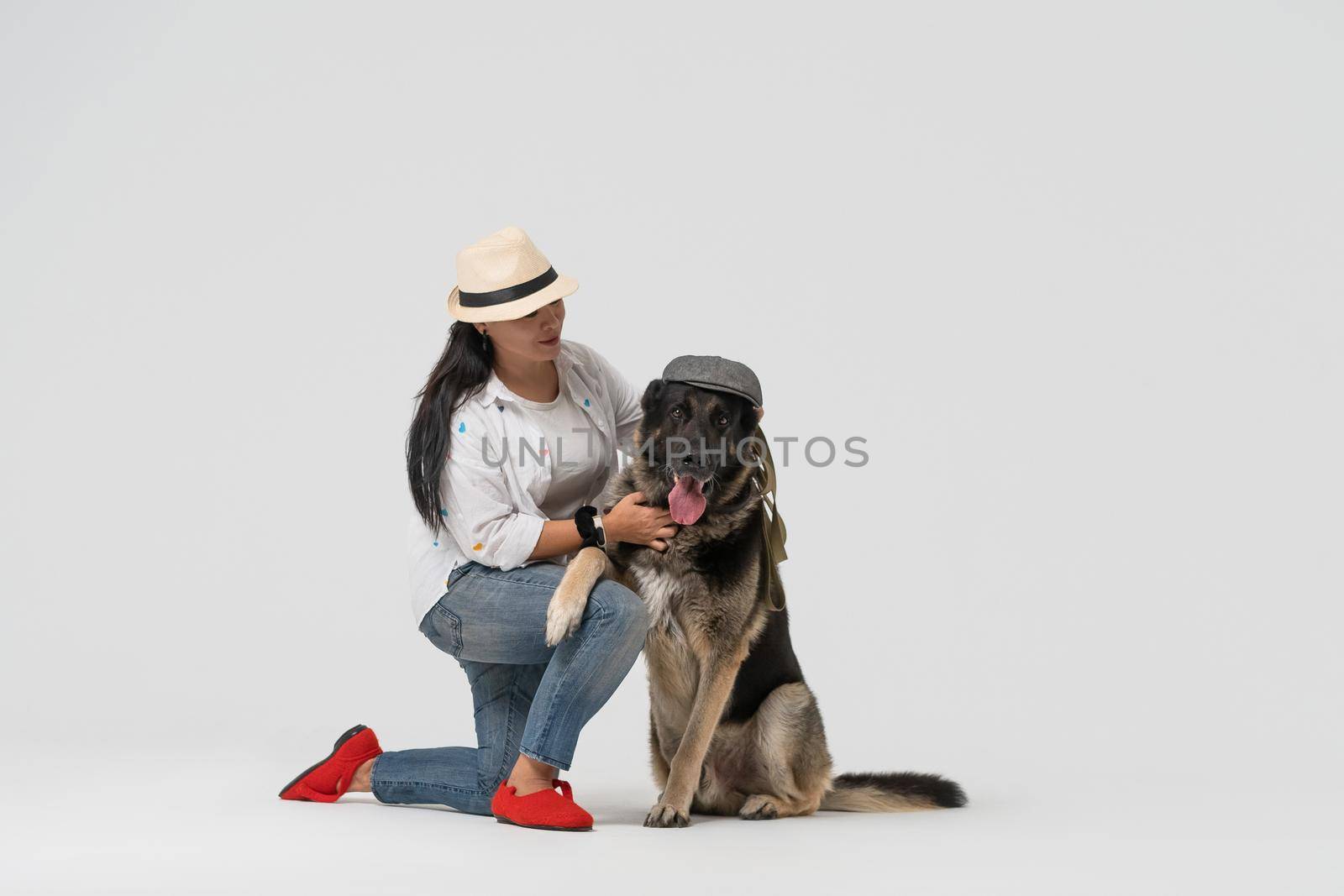 Woman in hat and Eastern European Shepherd wearing cap posing on white background. Pet concept.