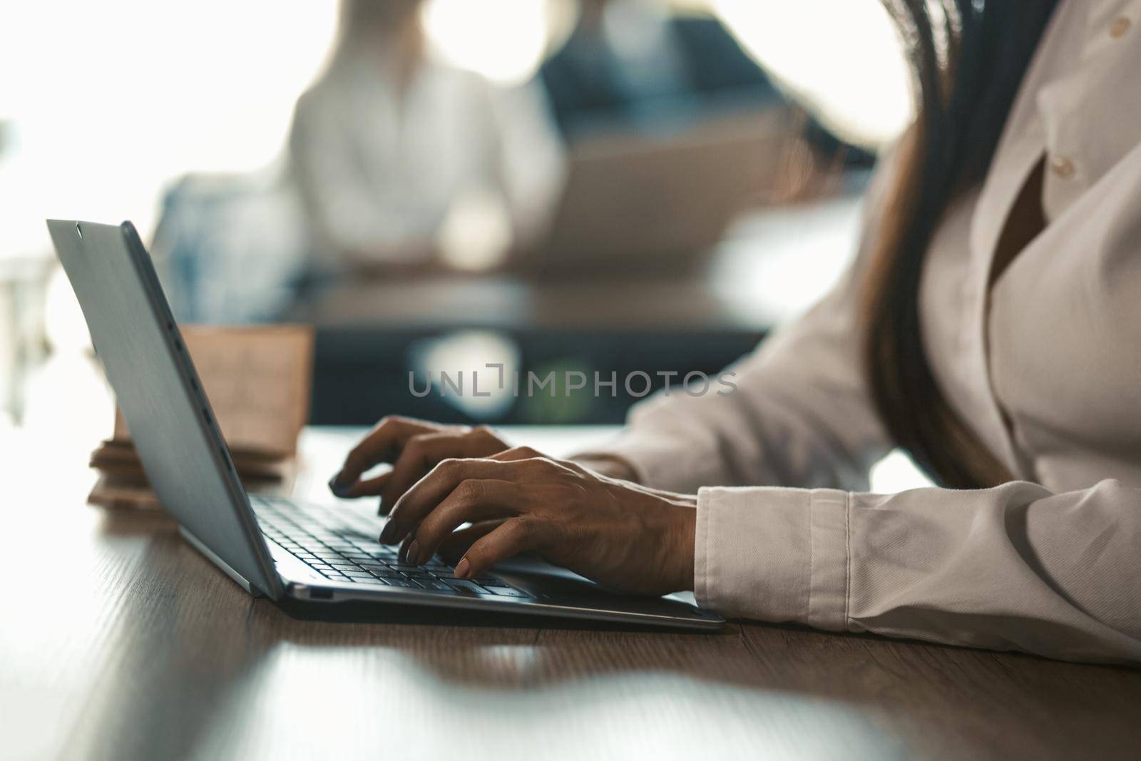 Office manager typing laptop keyboard. Coworkers working in office on blurred background. Toned image. Close up shot of female hands. High quality photo.