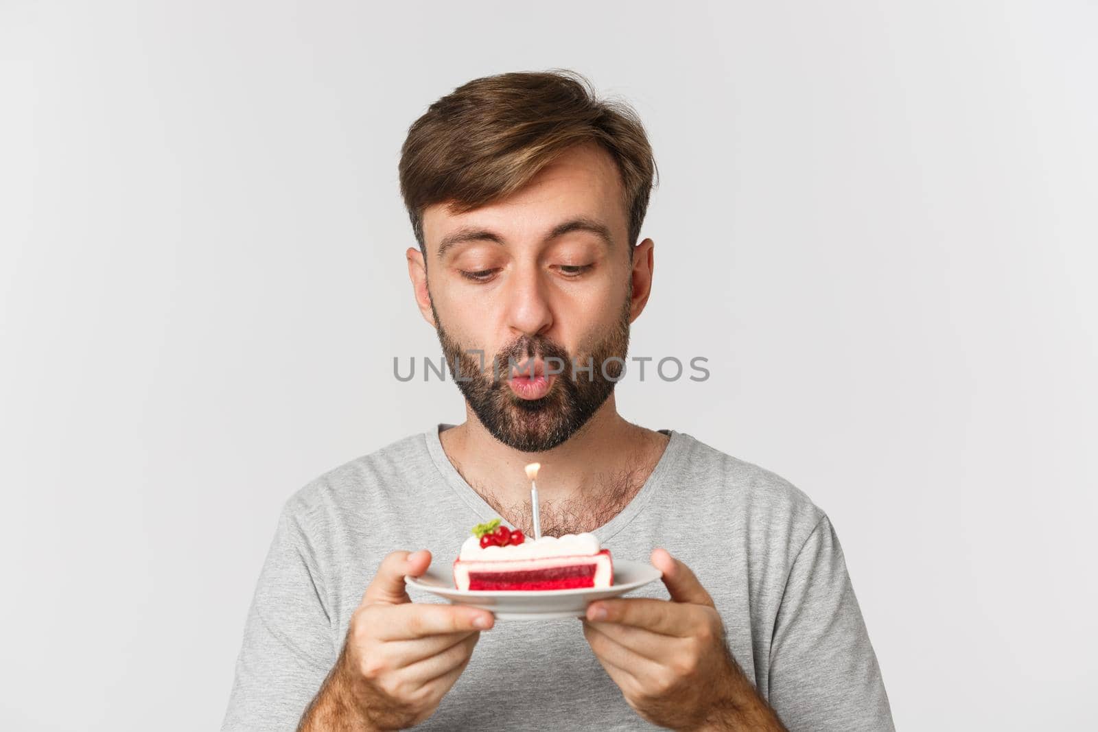 Close-up of happy bearded man, smiling and celebrating birthday, holding cake with lit candle, making b-day wish, standing over white background by Benzoix