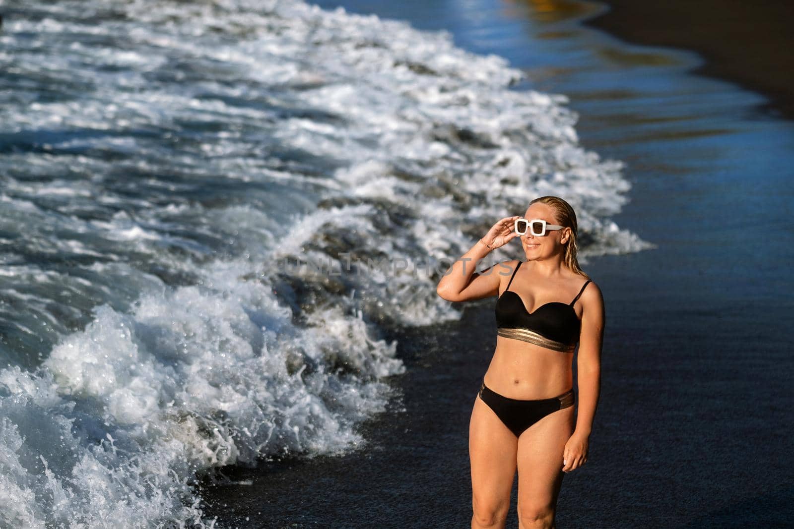 A girl in a black swimsuit walks on the beach on the island of Tenerife in the Atlantic Ocean, Spain.