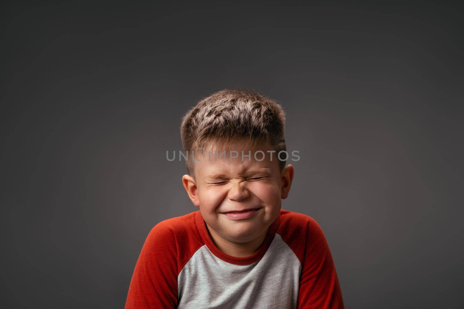 Funny boy smiles closed eyes. Isolated on gray background. Birthday surprise concept. Emotions concept. Copy spaces at both sides.