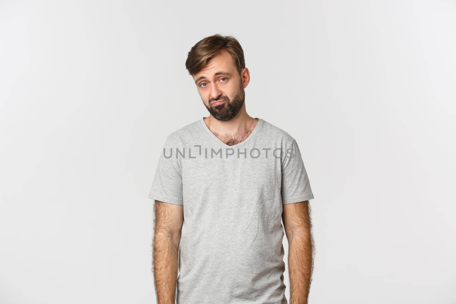 Portrait of sad and gloomy bearded man in gray t-shirt, frowning and looking miserable, standing over white background by Benzoix