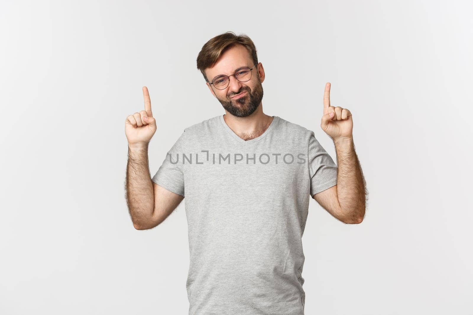 Skeptical and unamused bearded man smirking, pointing fingers up at something bad, showing logo, standing over white background by Benzoix