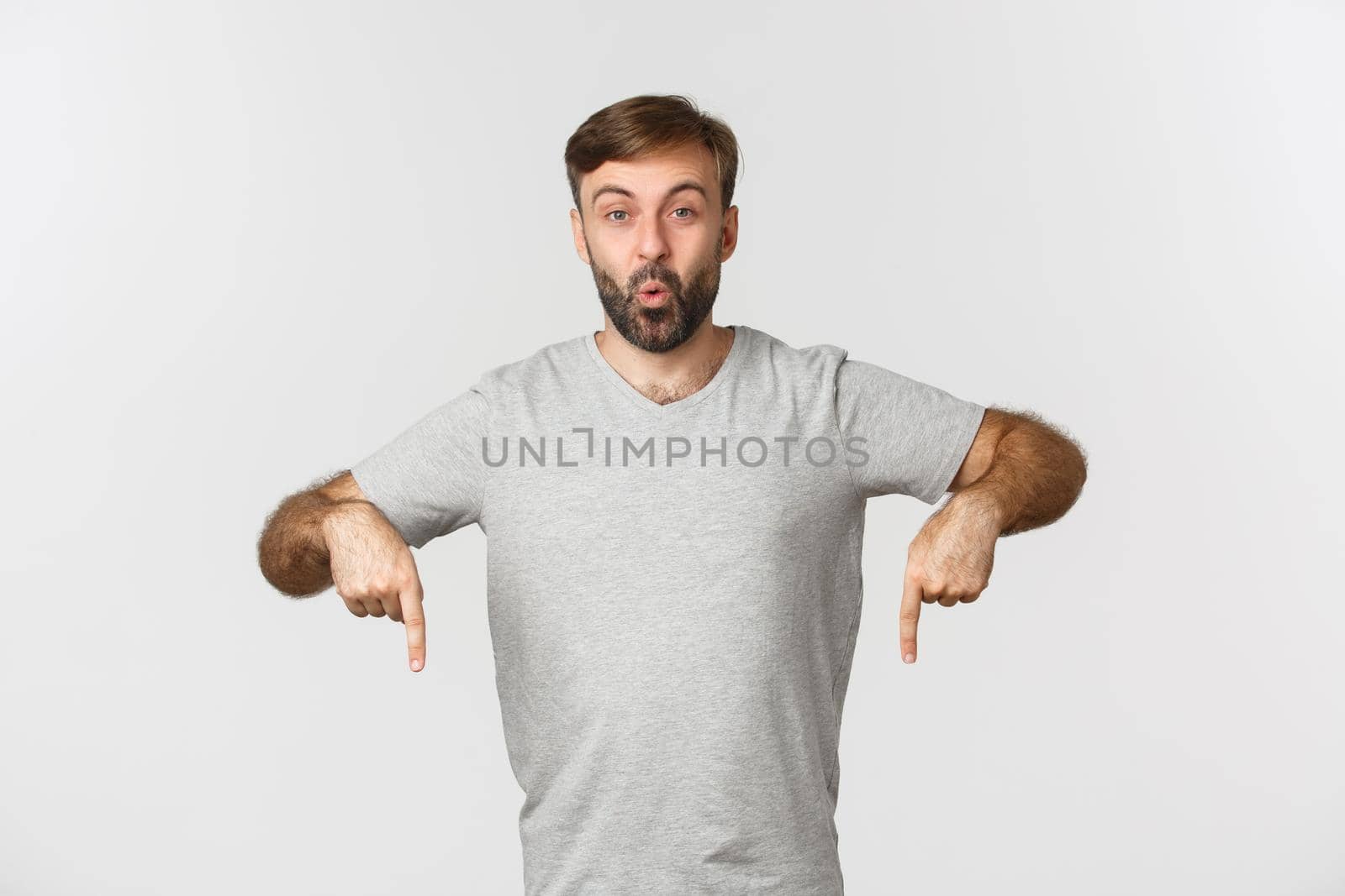 Portrait of excited guy with beard, pointing fingers down at something curious, showing logo, standing over white background by Benzoix