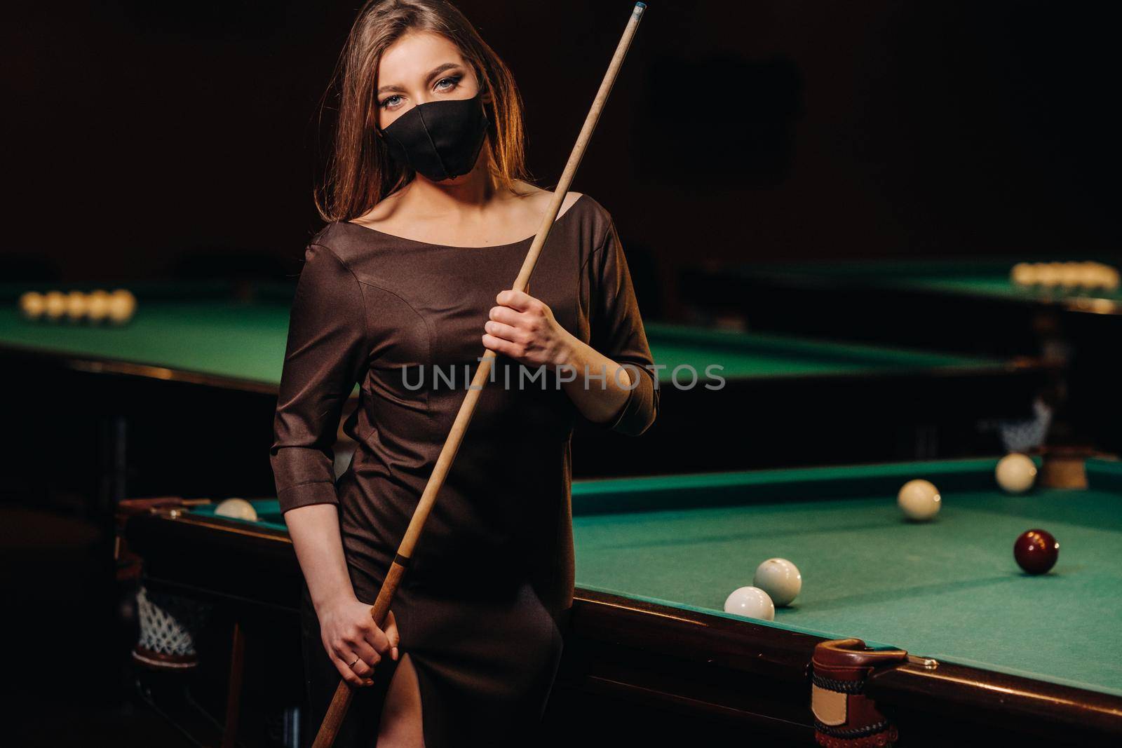 Masked girl in a pool club with a cue in her hands.