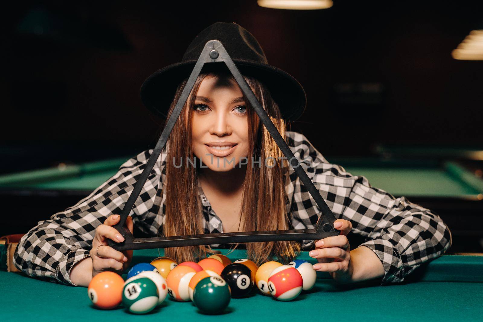 A girl in a hat in a billiard club with balls in her hands.Playing billiards.