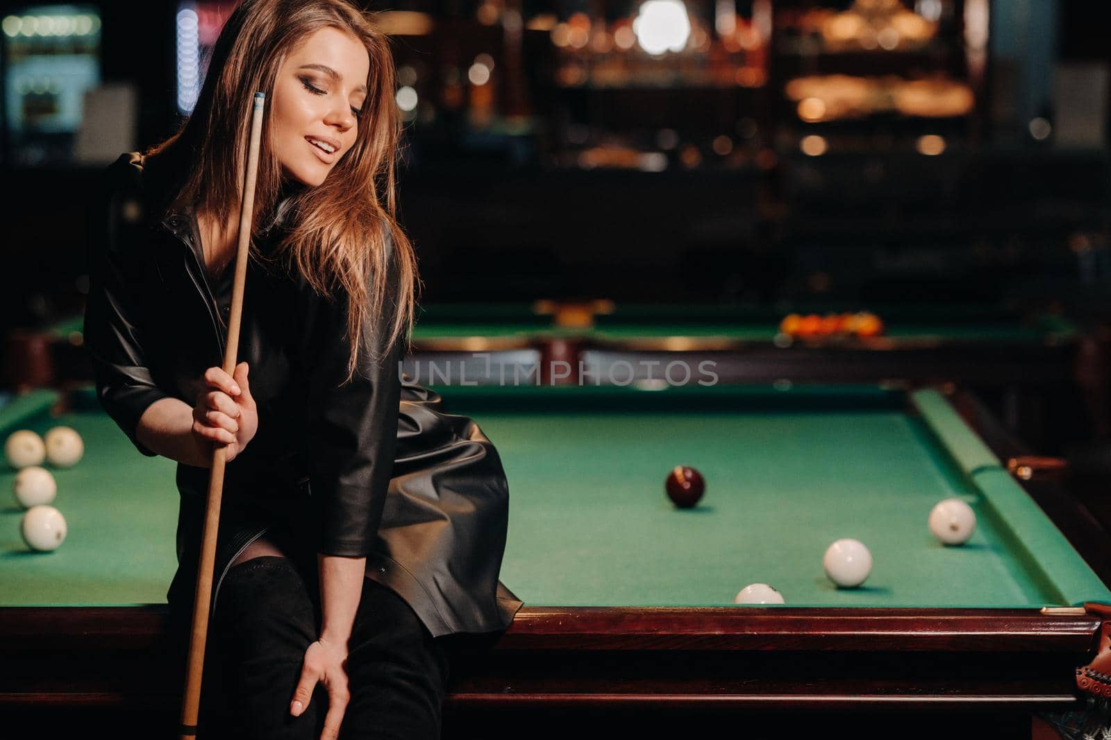 A girl with a cue in her hands sits on a table in a billiard club.Russian billiards by Lobachad