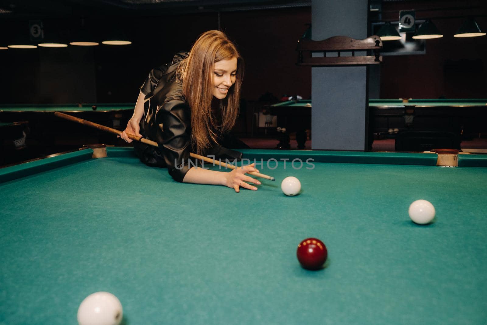 A girl with a cue in her hands makes a shot at a ball in a billiard club.Russian billiards by Lobachad