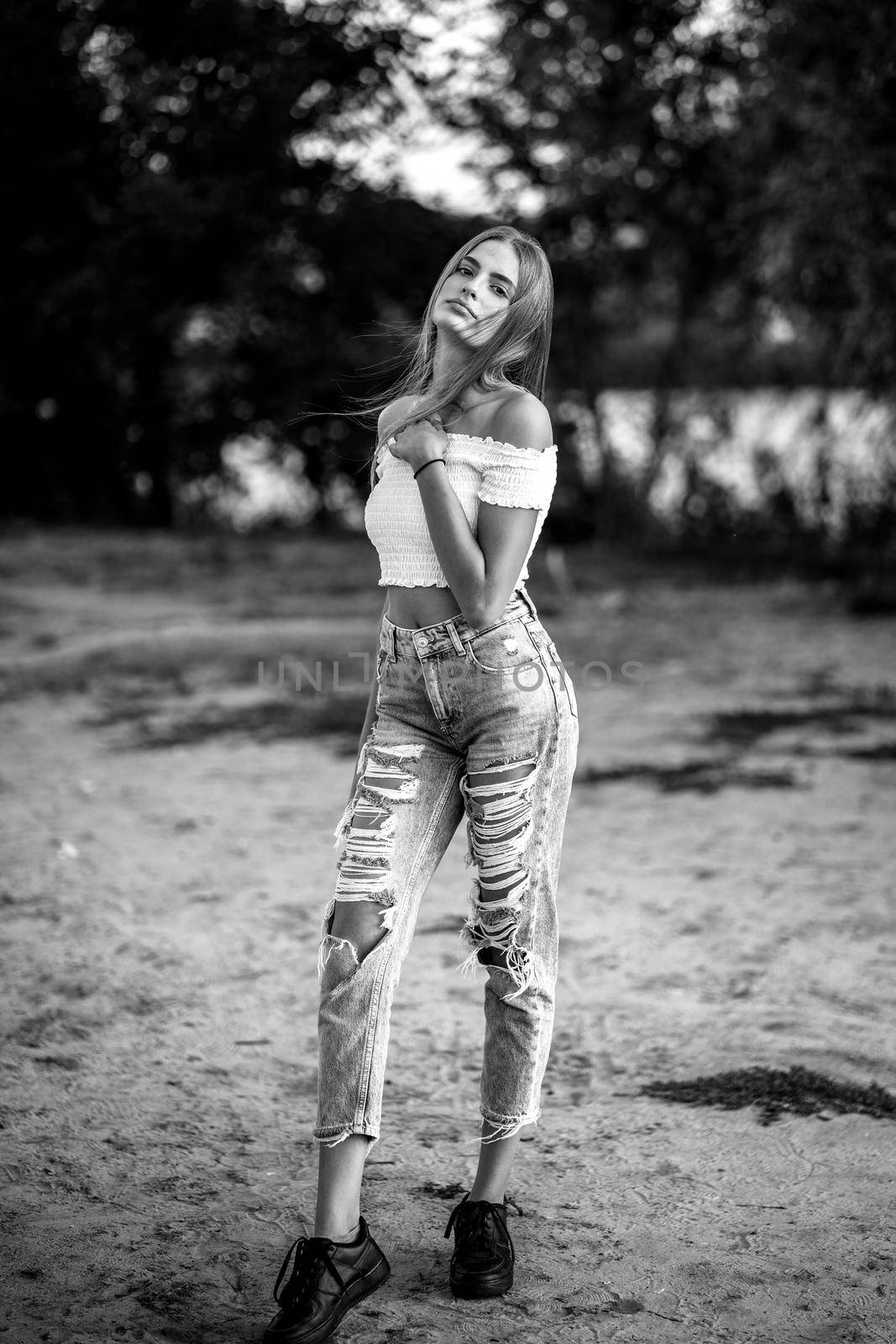 Beautiful teen girl posing full length against trees on blurred background at river side. Black and white image.