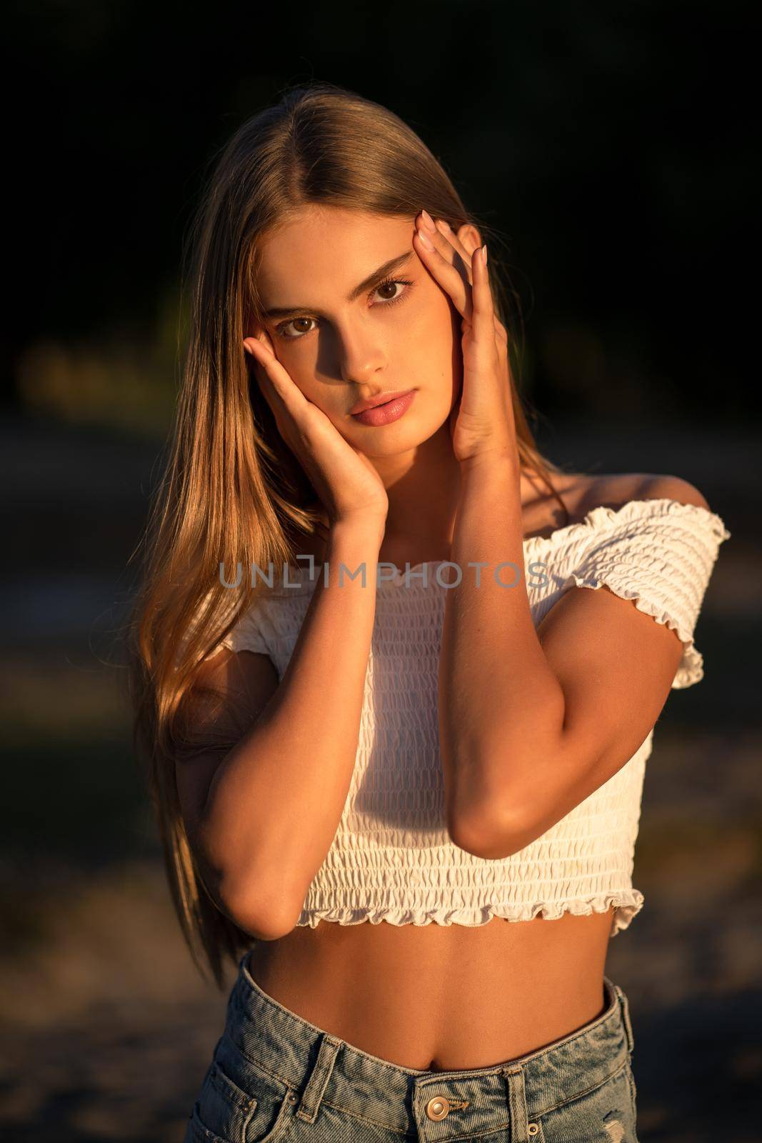 Portrait of teenage girl touching her face with her palms. Young Caucasian lady posing on sunset in nature. Skin care concept. Beauty concept.