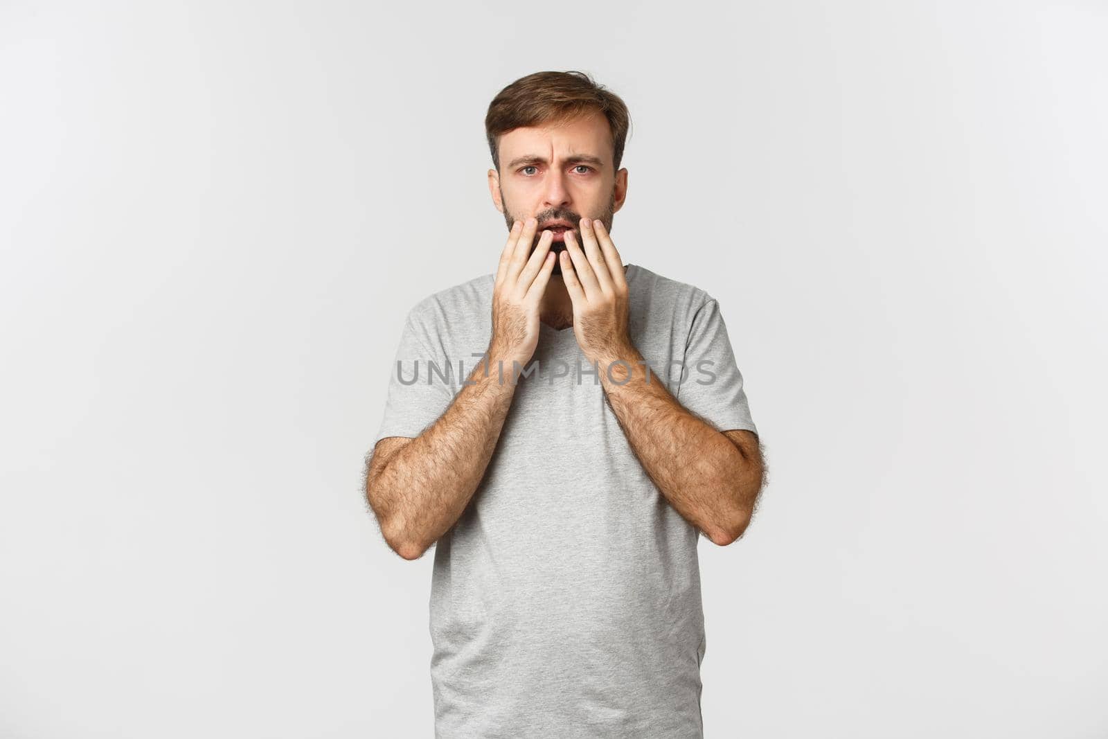 Portrait of shocked and worried guy staring at something disturbing, gasping and frowning, standing over white background by Benzoix