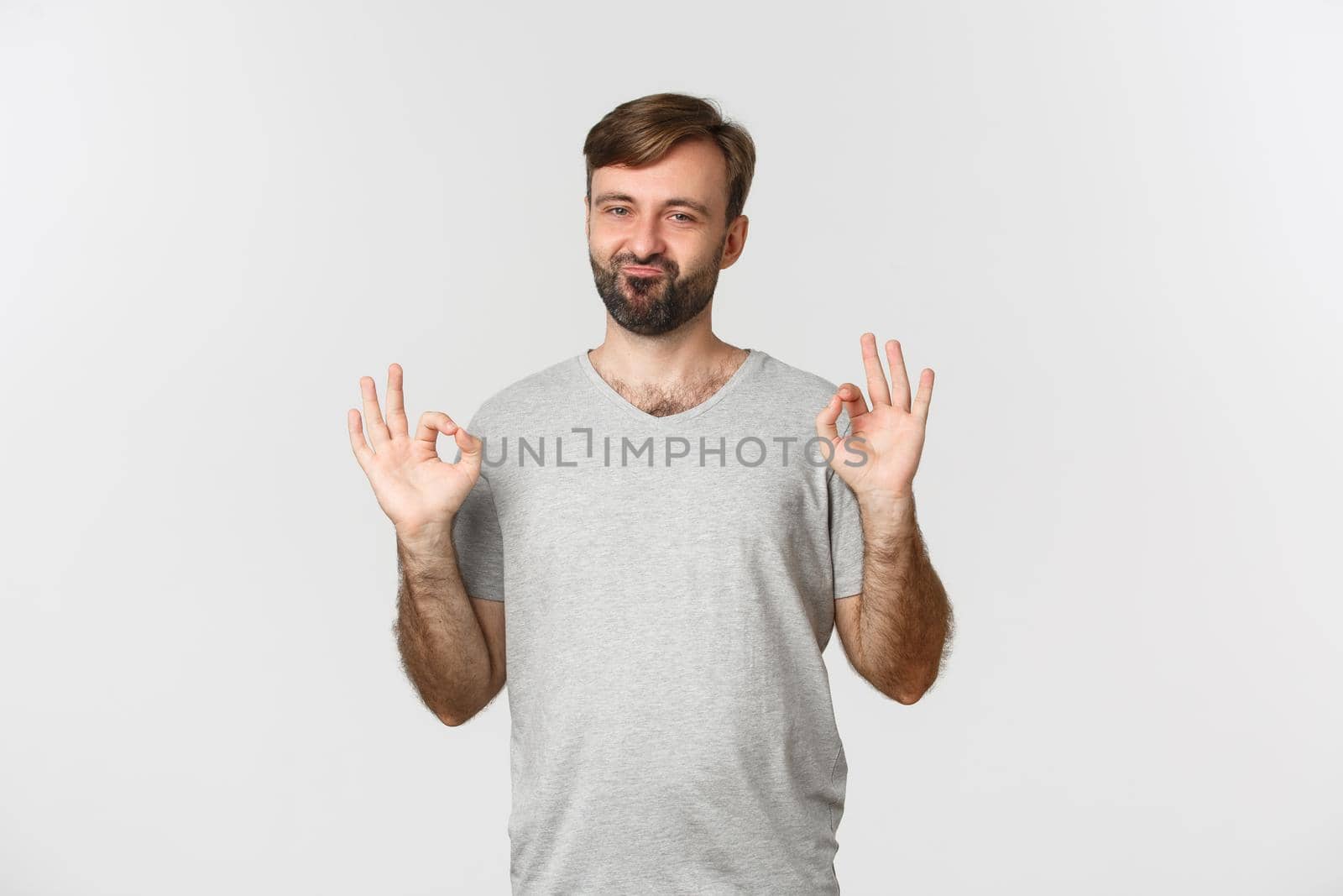 Portrait of satisfied handsome guy with beard, showing okay sign and approve something good, praising choice, standing over white background by Benzoix