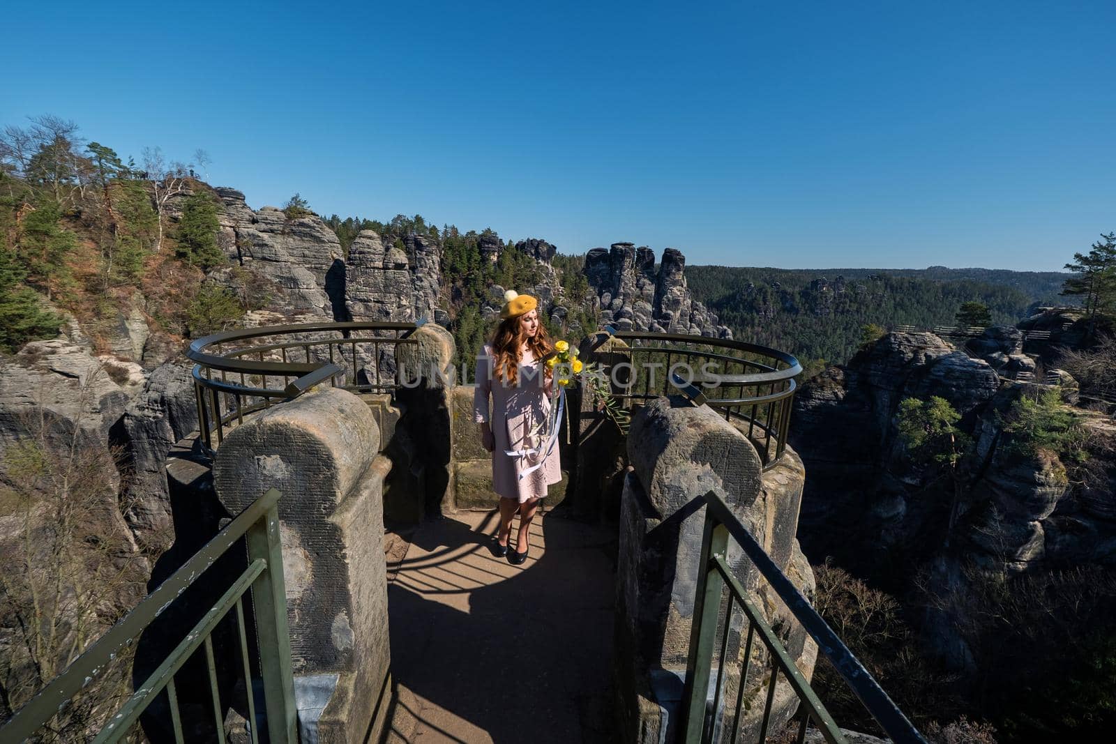 a girl in a gray coat and hat with a bouquet of flowers on the background of mountains and gorges in Swiss Saxony, Germany, Bastei.