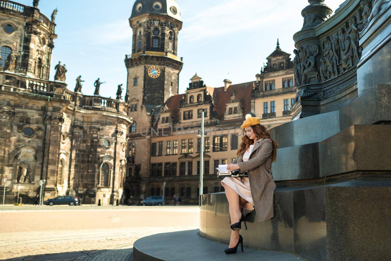 a girl in a coat and hat sits in the center of the old city of Dresden and types on a typewriter .Germany.