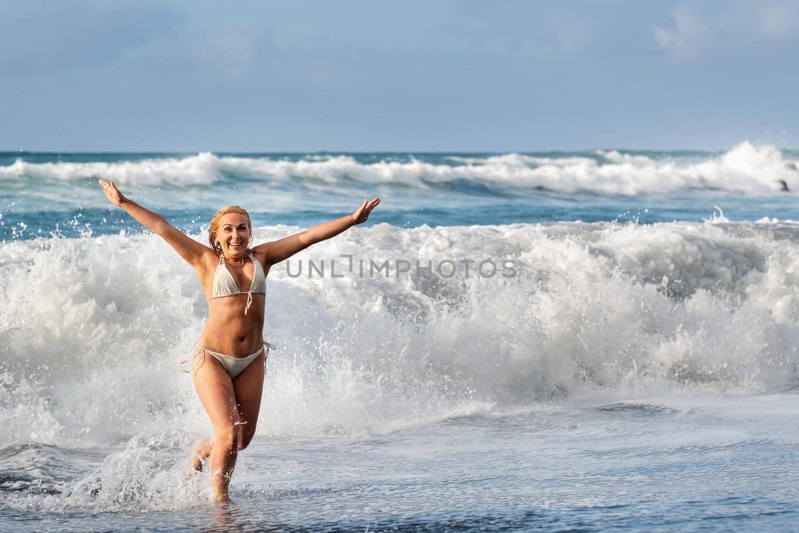 A girl with wet hair jumps over large waves in the Atlantic ocean, around a wave with splashes of spray and water drops.Tenerife.Spain by Lobachad